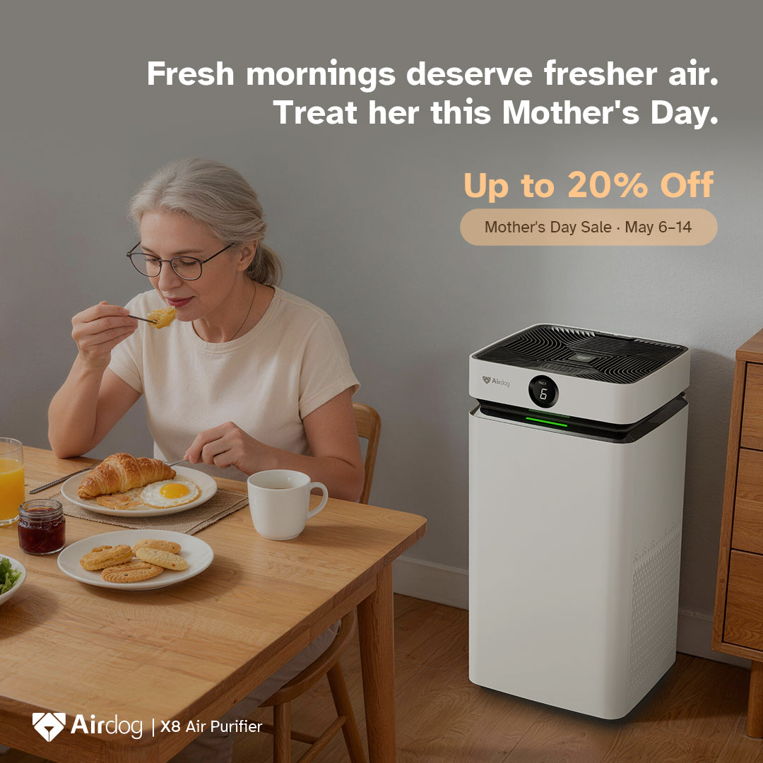 A woman eating breakfast at a wooden dining table next to a white and black Airdog X8 Air Purifier in a modern room. Text overlays advertise a Mother's Day sale on the Airdog brand.