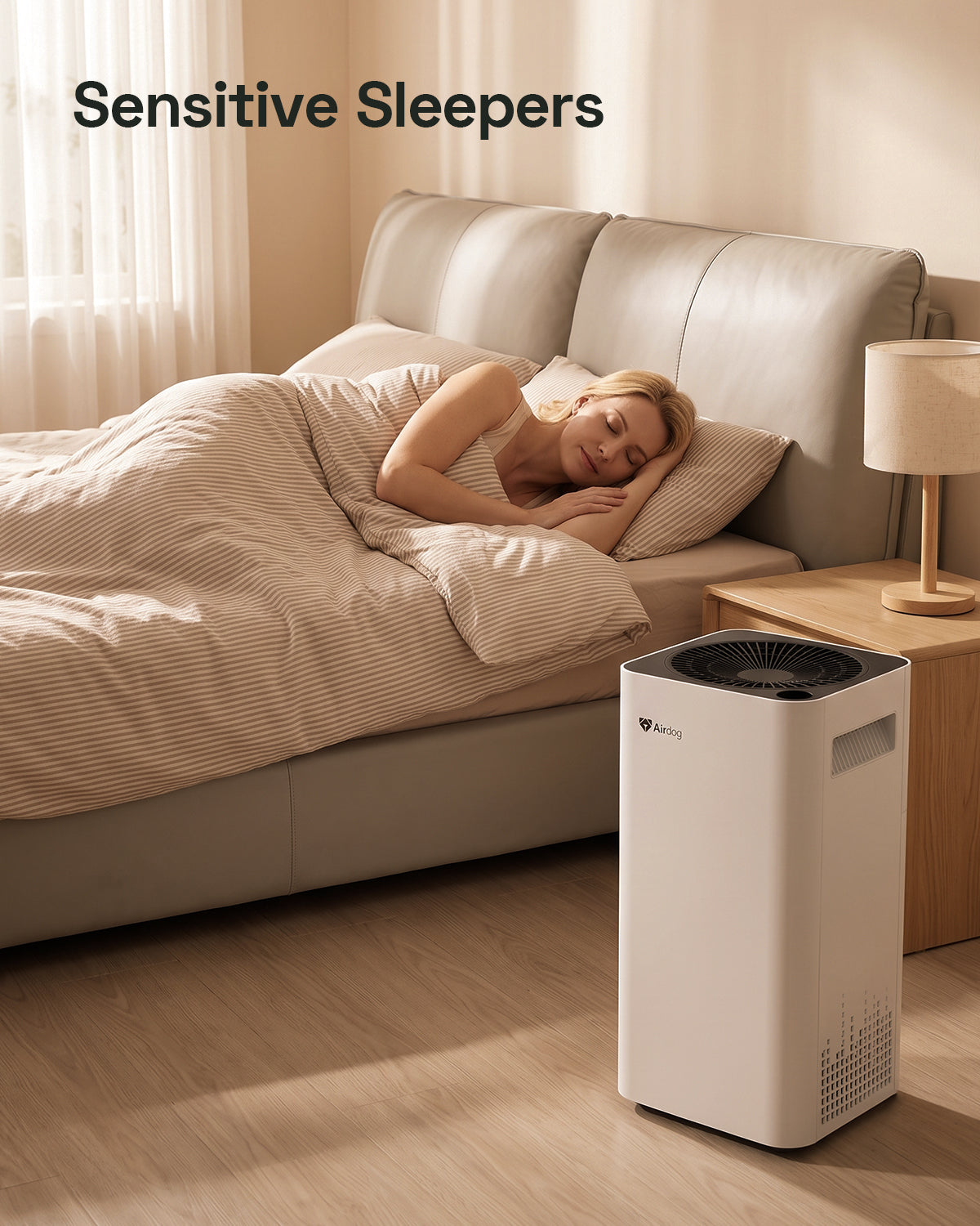 A white and black Airdog air purifier on a wooden floor next to a bed with a sleeping woman, in a warm, softly lit bedroom. The text 'Sensitive Sleepers' is displayed at the top left.
