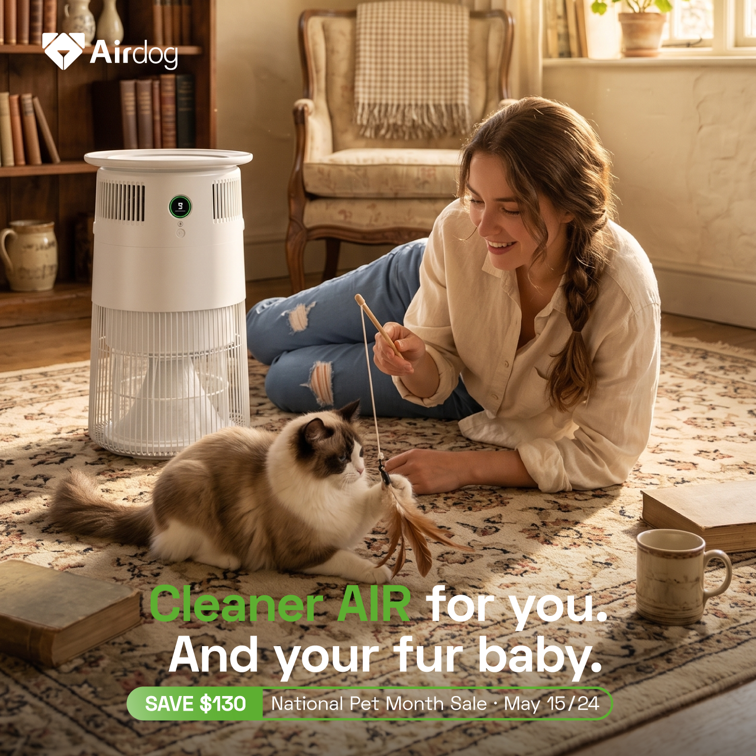 A woman lies on a patterned rug in a cozy living room, playing with a fluffy cat while holding a feather toy. A white Airdog pet air cleaner stands beside her, with promotional text at the bottom reading 'Cleaner AIR for you. And your fur baby. Save $130 National Pet Month Sale May 15/24'