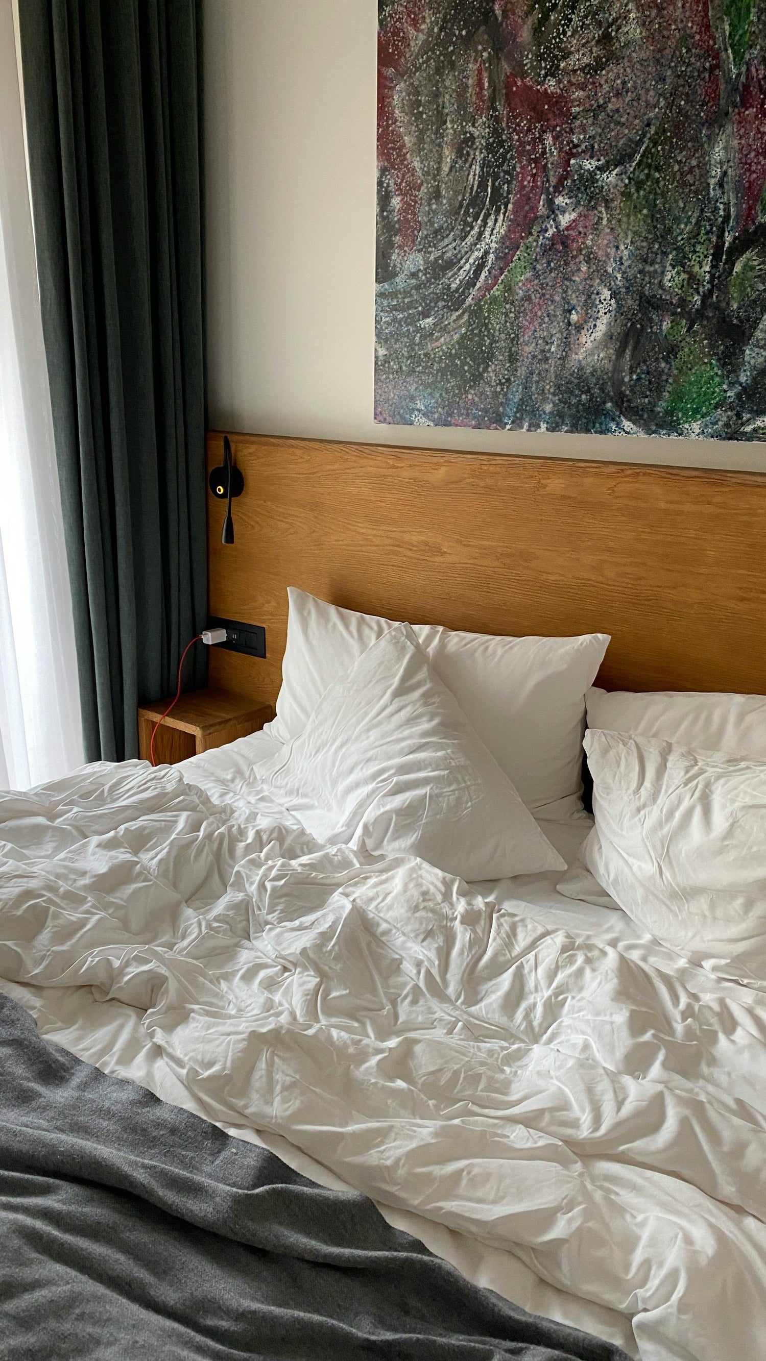 Bedroom with a bed featuring white bedding and a wooden headboard, with a colorful abstract painting on the wall.